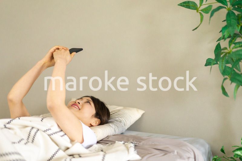 ベッドでスマホを使う若い女性