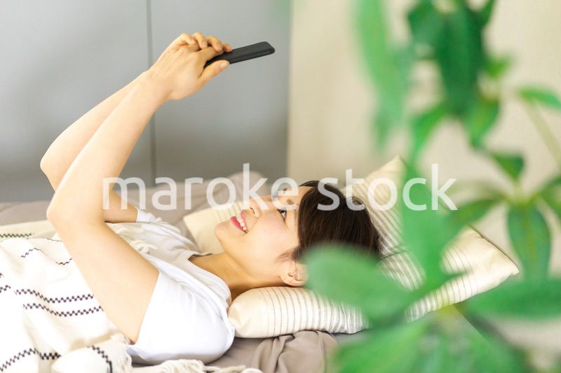 ベッドでスマホを使う若い女性