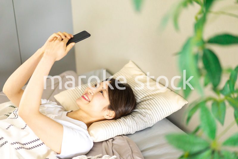 ベッドでスマホを使う若い女性