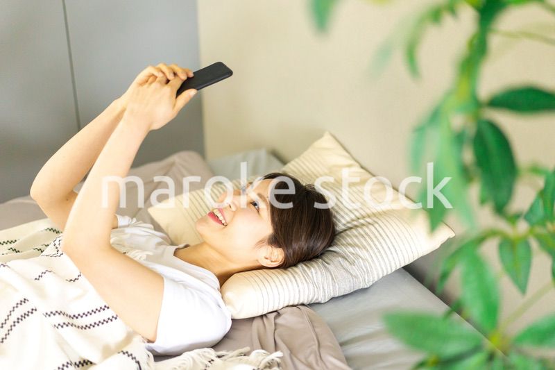 ベッドでスマホを使う若い女性