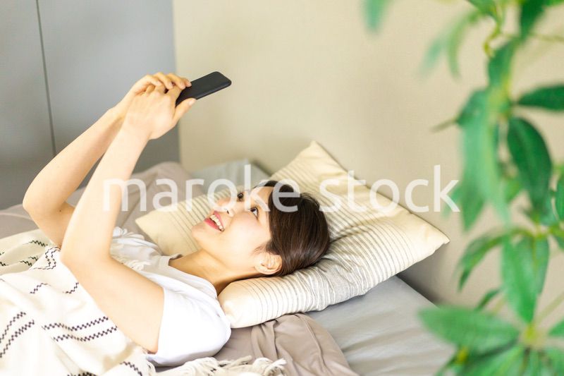 ベッドでスマホを使う若い女性