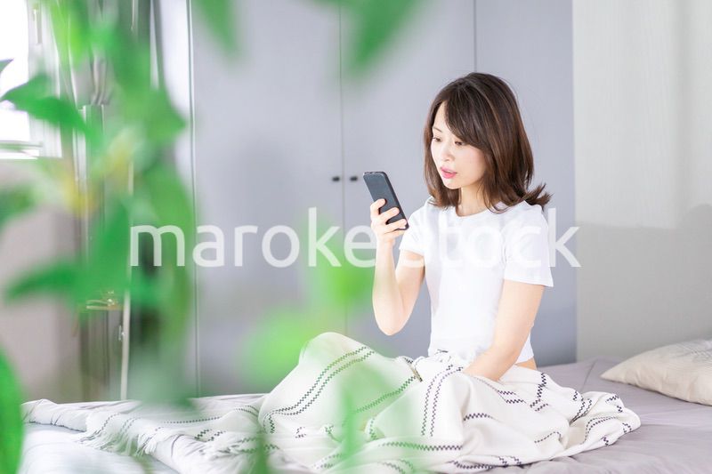ベッドでスマホを使う若い女性