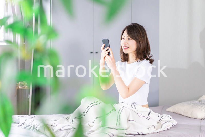 ベッドでスマホを使う若い女性