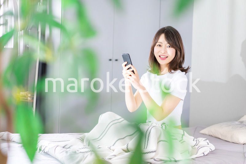 ベッドでスマホを使う若い女性