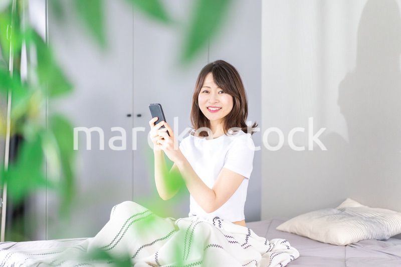 ベッドでスマホを使う若い女性