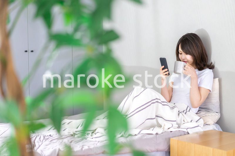 ベッドでスマホを使う若い女性