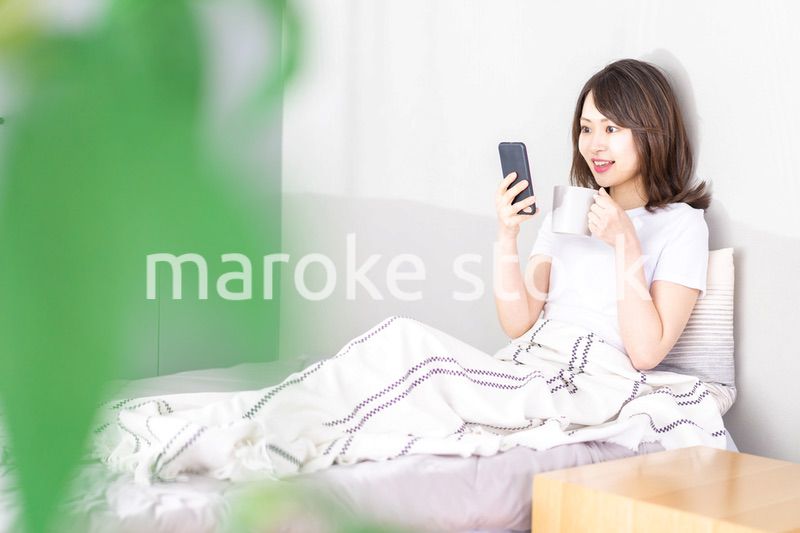 ベッドでスマホを使う若い女性