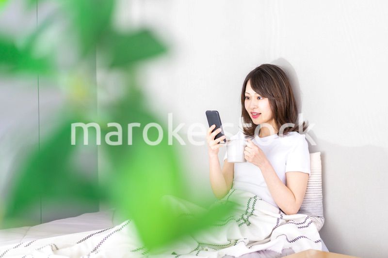 ベッドでスマホを使う若い女性