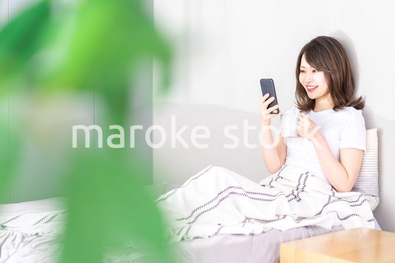 ベッドでスマホを使う若い女性