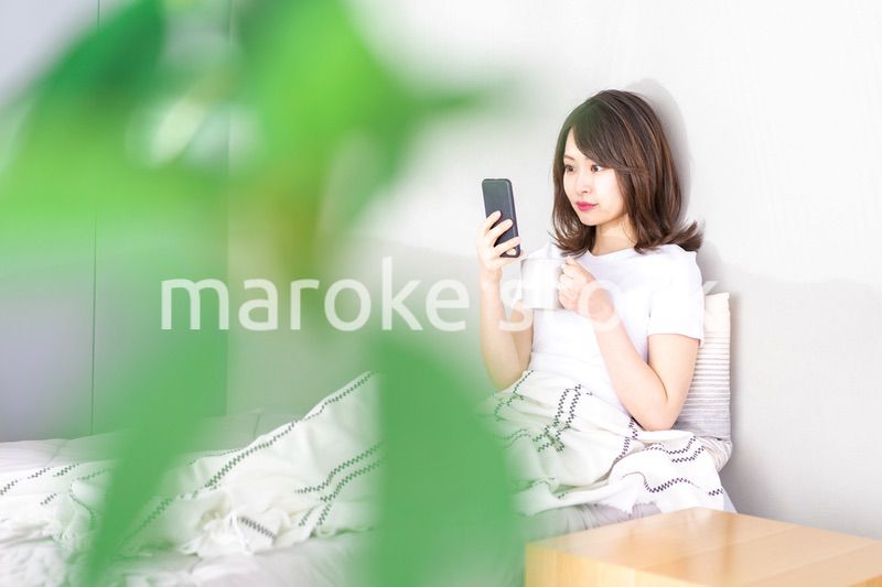 ベッドでスマホを使う若い女性