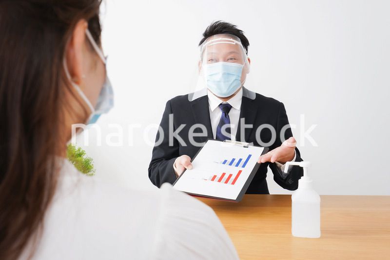 フェイスシールドとマスクをして商談をするビジネスパーソン