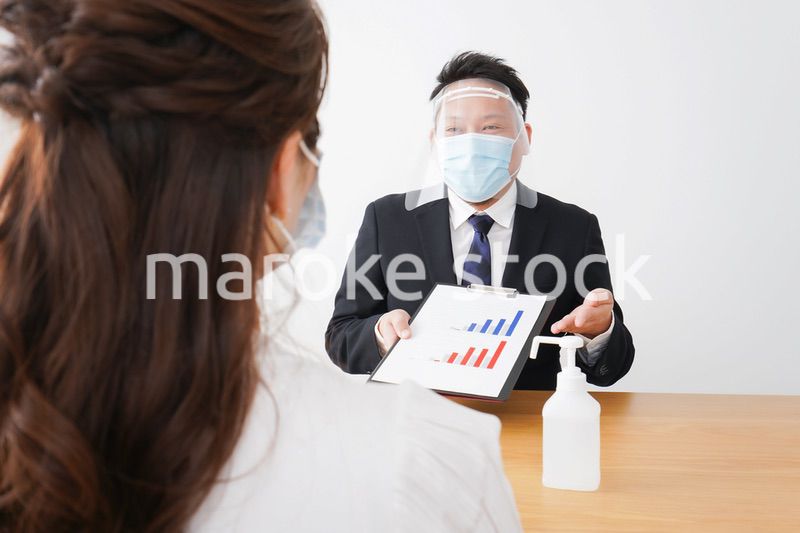 フェイスシールドとマスクをして商談をするビジネスパーソン