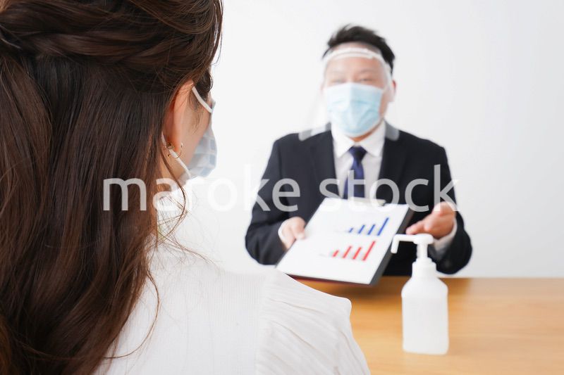 フェイスシールドとマスクをして商談をするビジネスパーソン