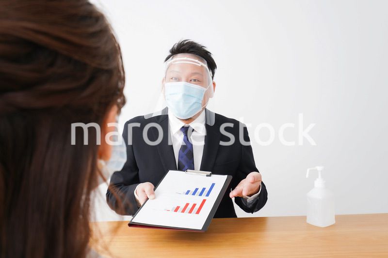 フェイスシールドとマスクをして商談をするビジネスパーソン