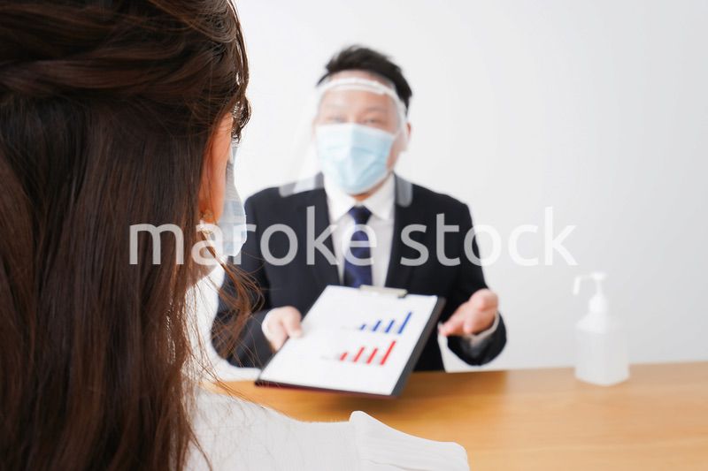 フェイスシールドとマスクをして商談をするビジネスパーソン
