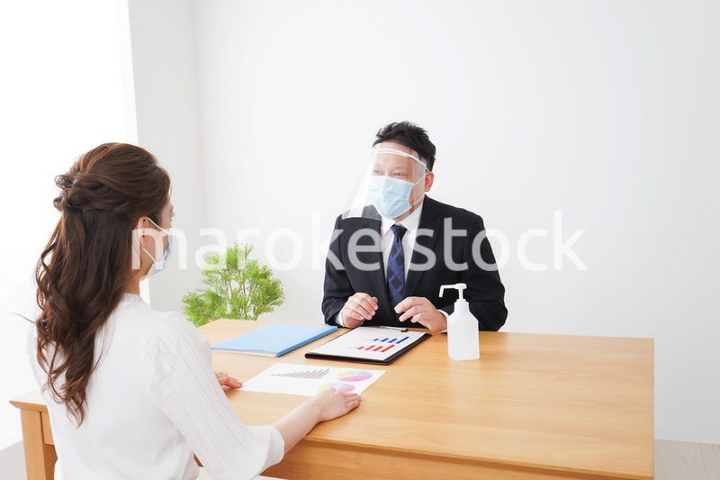 フェイスシールドとマスクをして商談をするビジネスパーソン