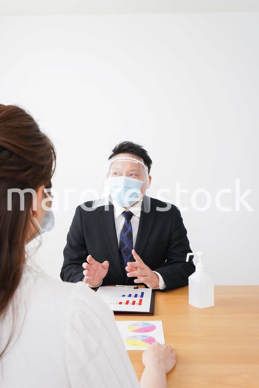 フェイスシールドとマスクをして商談をするビジネスパーソン