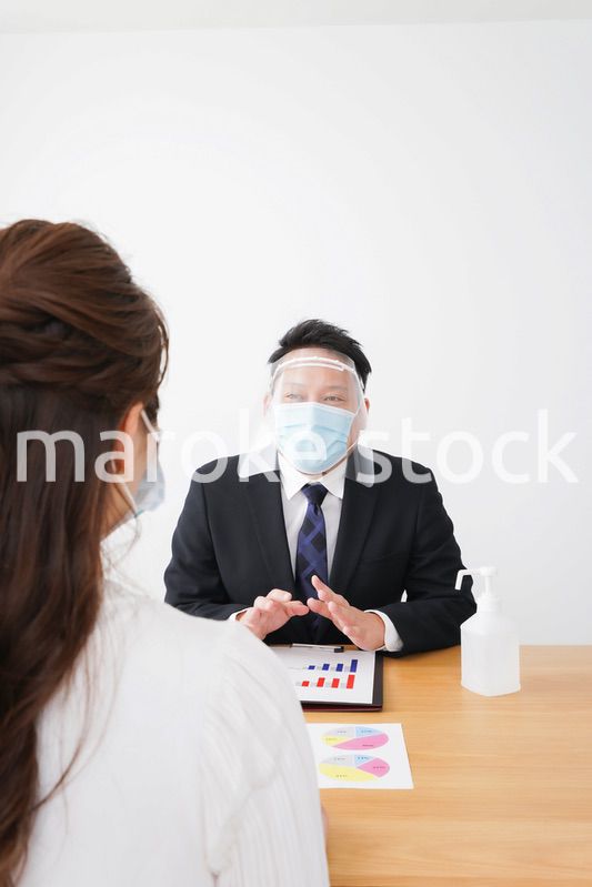 フェイスシールドとマスクをして商談をするビジネスパーソン