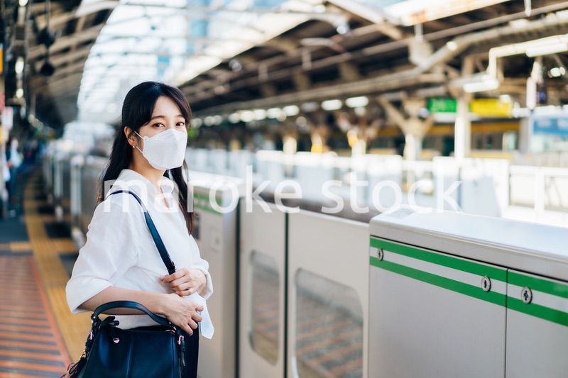マスクをして電車を待つ若い女性