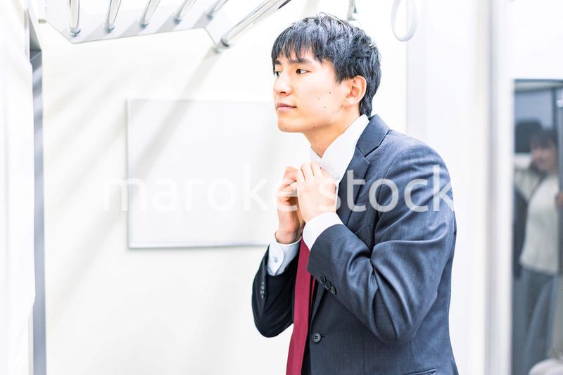 電車内でネクタイを締める男性