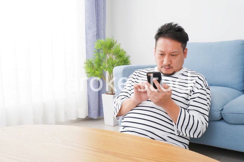 部屋でスマホを使う男性