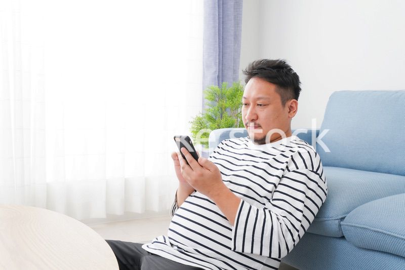 部屋でスマホを使う男性