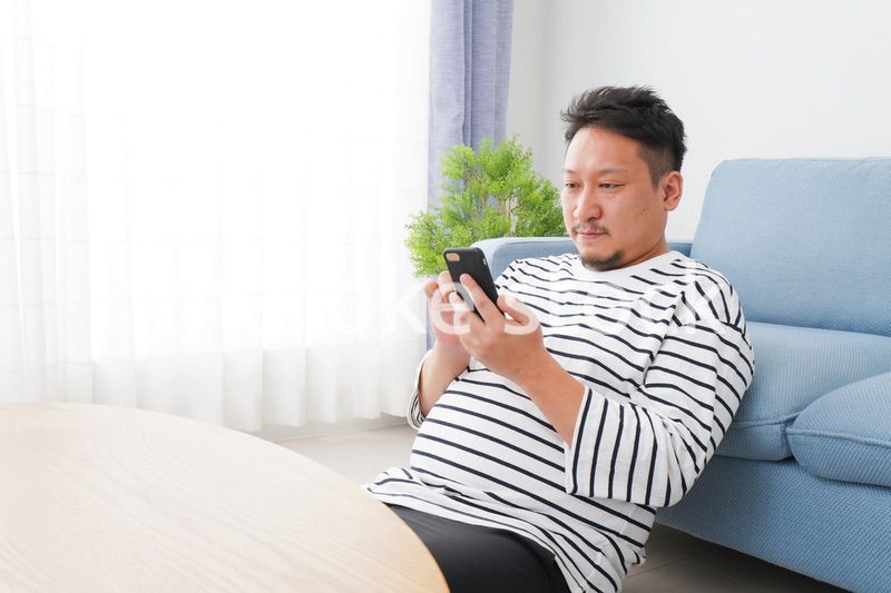 部屋でスマホを使う男性