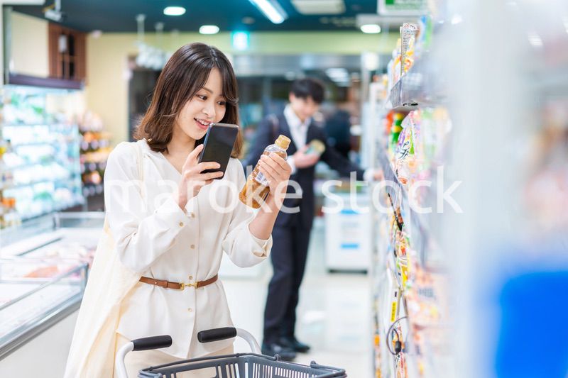 スーパーの商品をスマホで調べる若い女性