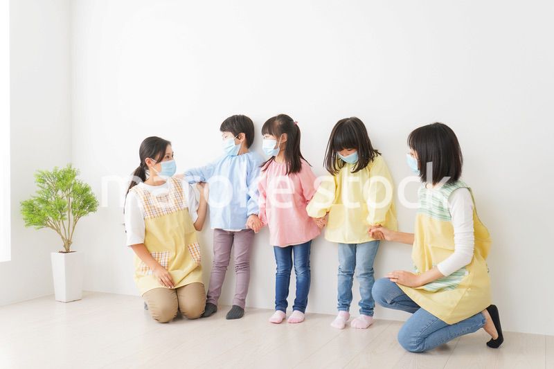 マスクを付けて幼稚園で遊ぶ子どもたちの先生